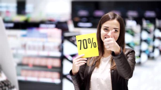 化妆品商店的女人表现出拇指和折扣标志，大甩卖，她震惊了