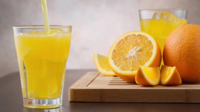 将橙汁倒入玻璃杯中，背景是新鲜的橙色水果