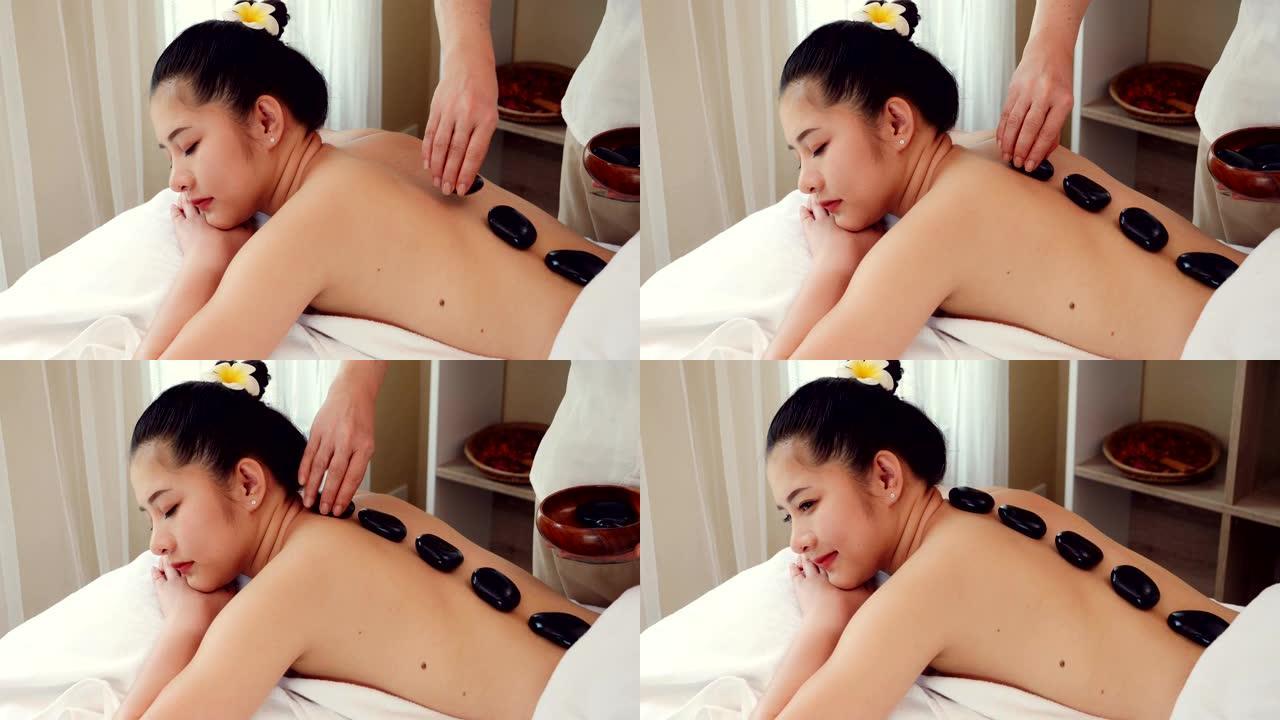 亚洲女性放松，同时接受专业按摩师的美容和健康按摩。按摩师用热石头按摩亚洲女性的身体