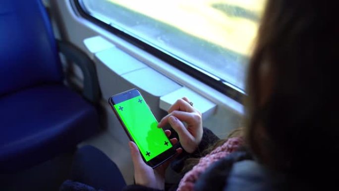 坐火车旅行时，女孩手持绿屏智能手机的俯视图。乘客女性在互联网上浏览，使用导航仪并坐在窗户附近。智能手