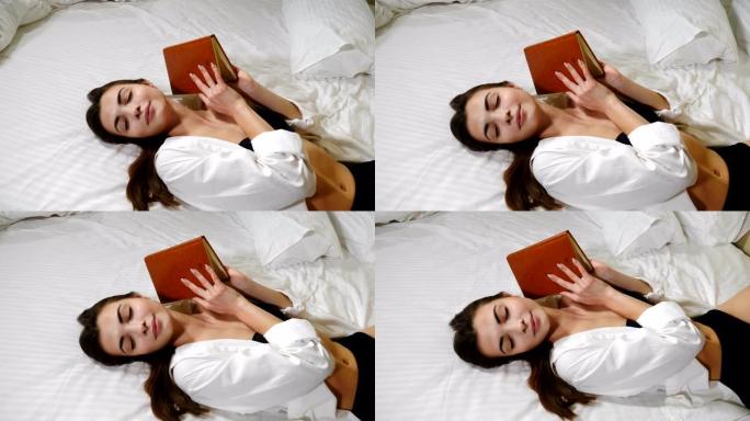 美丽的年轻女士躺在大床上，手里拿着纸条在家放松。酒店房间里迷人的女人躺在白色床上，闭着眼睛。出差。4