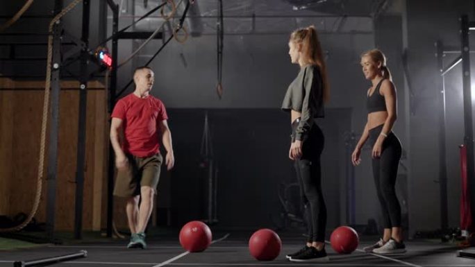 教练在健身房。一个男人向两个年轻女人展示练习。金发女郎学习正确的锻炼技巧