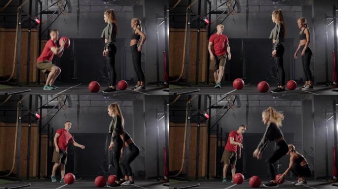 教练在健身房。一个男人向两个年轻女人展示练习。金发女郎学习正确的锻炼技巧