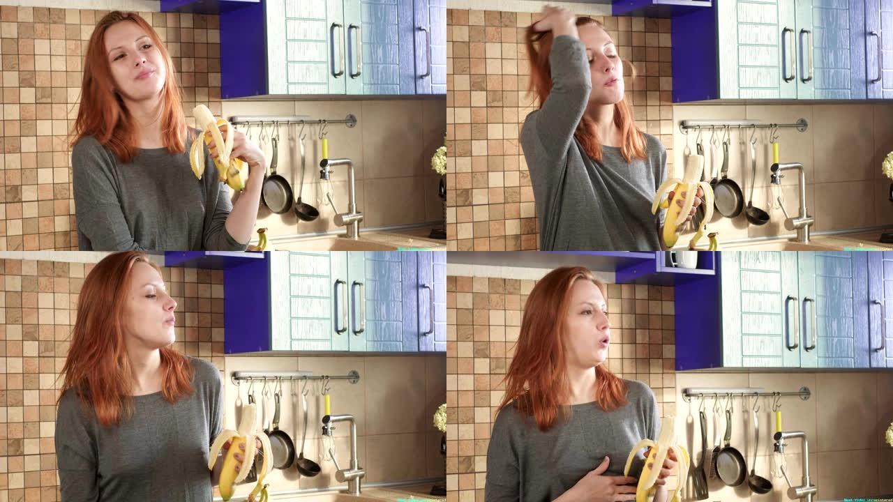 迷人的饥饿的红发女孩在周末的清晨在厨房里吃一个大香蕉。清洗果皮。健康饮食，正确的生活方式。运动早餐。