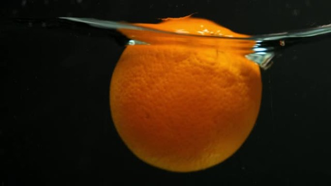 橙色水果以慢动作落在水中。在黑色背景上。
