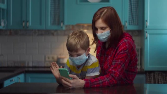 30多岁的母亲和男孩戴着医用口罩与亲戚通过手机在线交谈，挥手致意。家庭在病毒的自我隔离。停止流行。