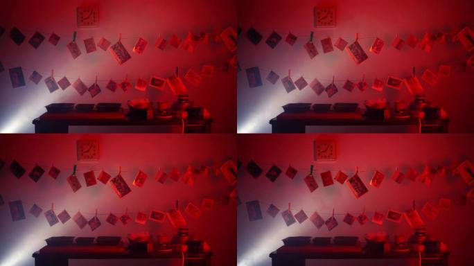 照片实验室的红色暗室，显影后挂在绳子上的老照片。在黑暗的房间里投射一束光，旁边是一堆未拆光的卷轴。更