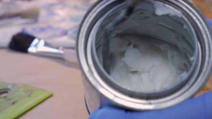 画家从小罐中刮掉冷蜡或糊状介质
