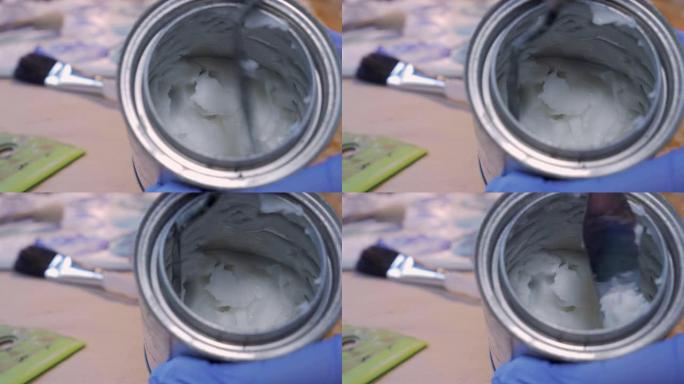 画家从小罐中刮掉冷蜡或糊状介质