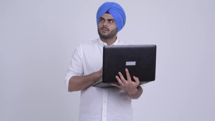 快乐的年轻大胡子的印度锡克教徒在使用笔记本电脑时带着头巾思考