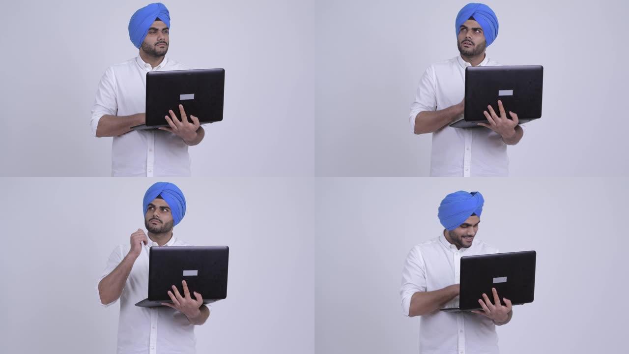 快乐的年轻大胡子的印度锡克教徒在使用笔记本电脑时带着头巾思考