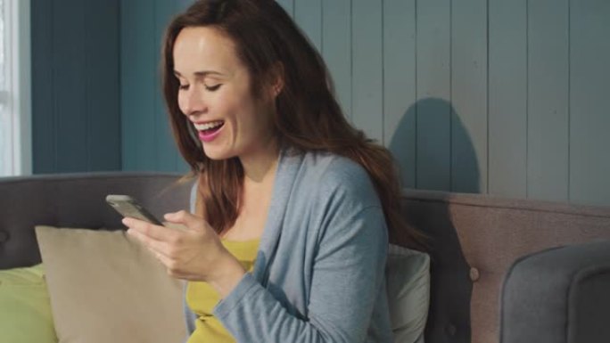 宏观笑孕妇在现代客厅的智能手机屏幕上看。