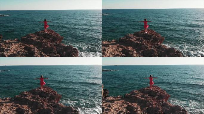 女人的轮廓，双手分开，站在岩石悬崖上，靠着太阳和太阳路。穿着红色连衣裙的女孩双臂分开在风中拍打，站在
