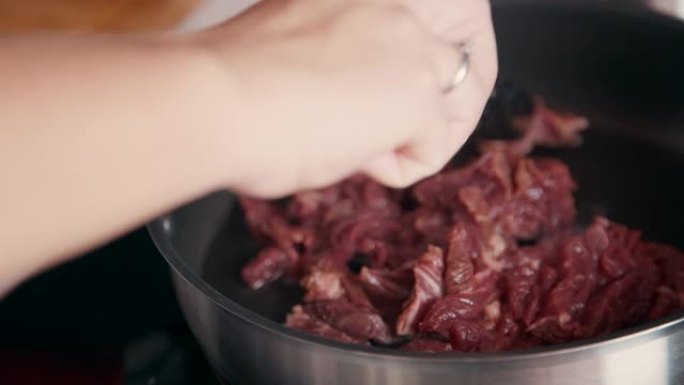 厨师手的特写镜头，将切成薄片的肉放在煎锅上。女人煮牛肉