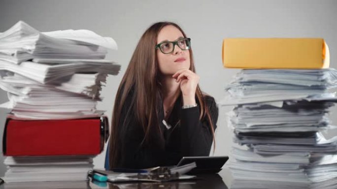 桌子上有一堆未完成的文件和文件，彩色的文件夹和戴着眼镜沉思的女会计。商业工作者思考计算和财务报告。分