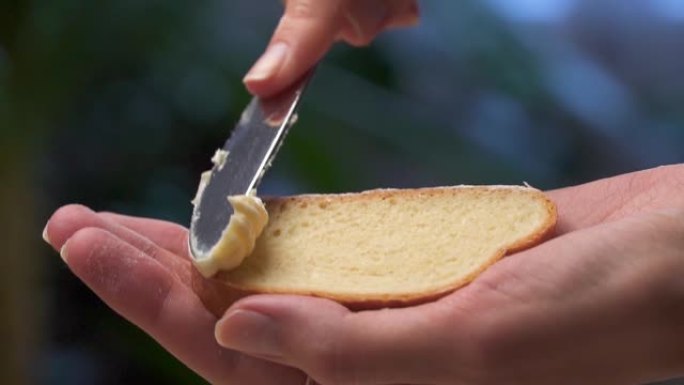 一只雌性手用刀在白面包上涂抹黄油。