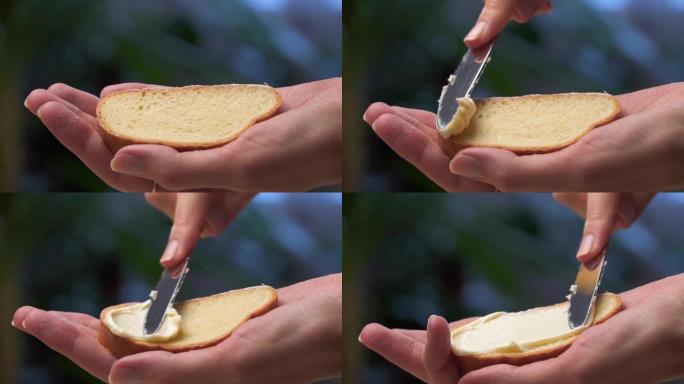 一只雌性手用刀在白面包上涂抹黄油。