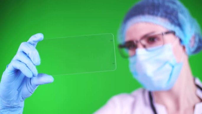 绿色背景。特写镜头，医生穿着医疗帽、口罩、蓝色医用手套，拿着一张玻璃卡片，点击一下。可以在卡片上放置