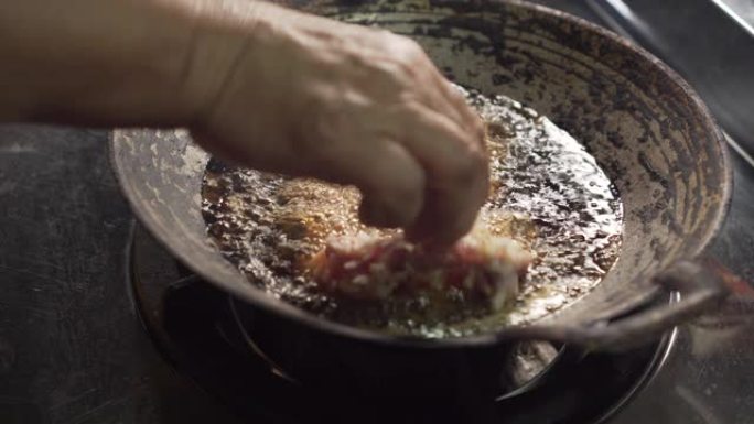 老太太把生鸡肉放在锅里，用煮油。做炸鸡。静态镜头。