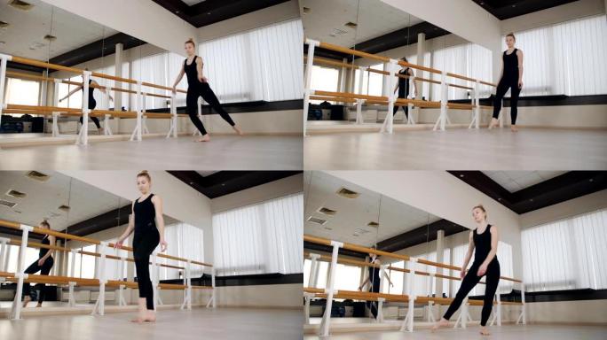 优雅的古典芭蕾舞演员穿着运动服，在舞蹈工作室的芭蕾巴雷练习站立分开的伸展姿势。