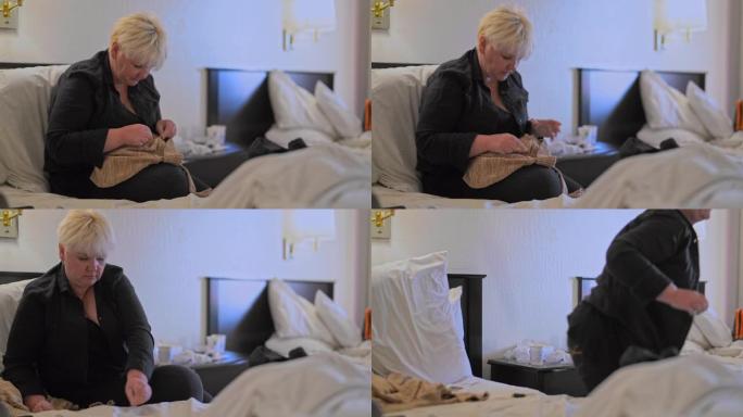 成熟的白人白人身体积极迷人的女人修理毛衣，在旅途中坐在汽车旅馆房间的床上。