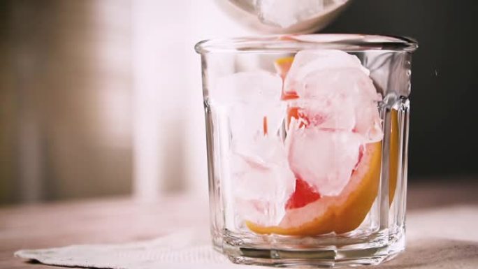 冰块与一块葡萄柚一起落入玻璃中，动作缓慢。葡萄柚鸡尾酒，特写。