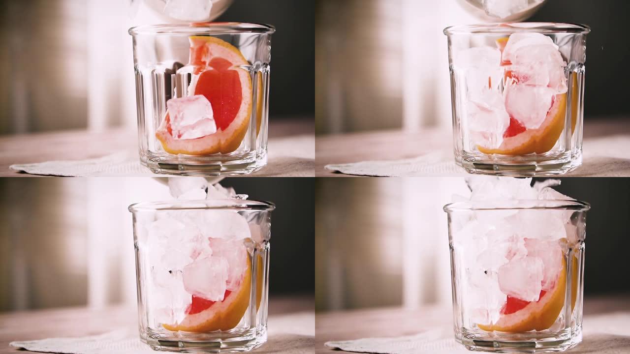 冰块与一块葡萄柚一起落入玻璃中，动作缓慢。葡萄柚鸡尾酒，特写。
