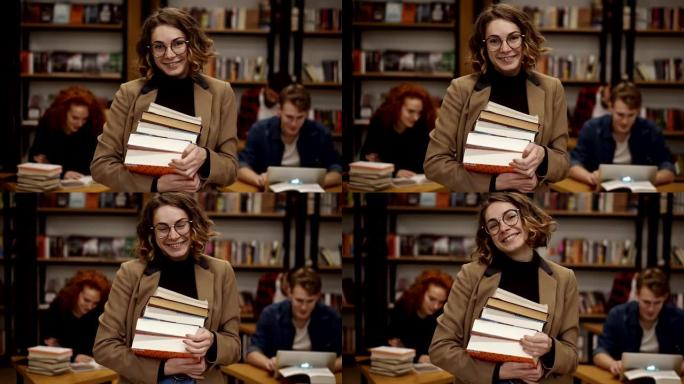 迷人的欧洲女学生在高中图书馆拿着书的肖像微笑着看着相机。教育、文学和人民观念。背景模糊的同学