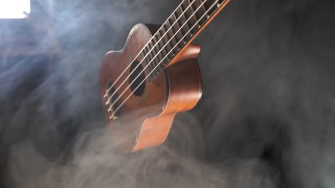 红木夏威夷四弦琴吉他孤立在黑色背景下，有烟