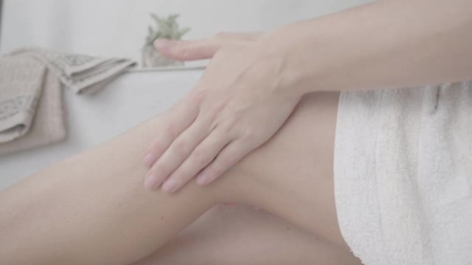 4k平的未分级特写镜头，一个女人在她的设计浴室里，用白毛巾用柔和的心情按摩她的腿