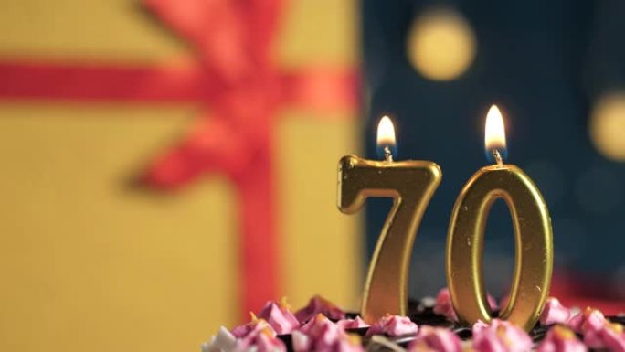 生日蛋糕70号点火器燃烧的金色蜡烛，蓝色背景礼物黄色盒子用红丝带绑起来。特写和慢动作