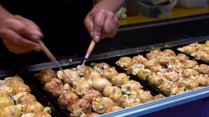 厨师手在章鱼锅烹饪日本小吃章鱼烧的4k特写镜头，在日本东京街头食品市场出售。男子手工准备日本传统美食