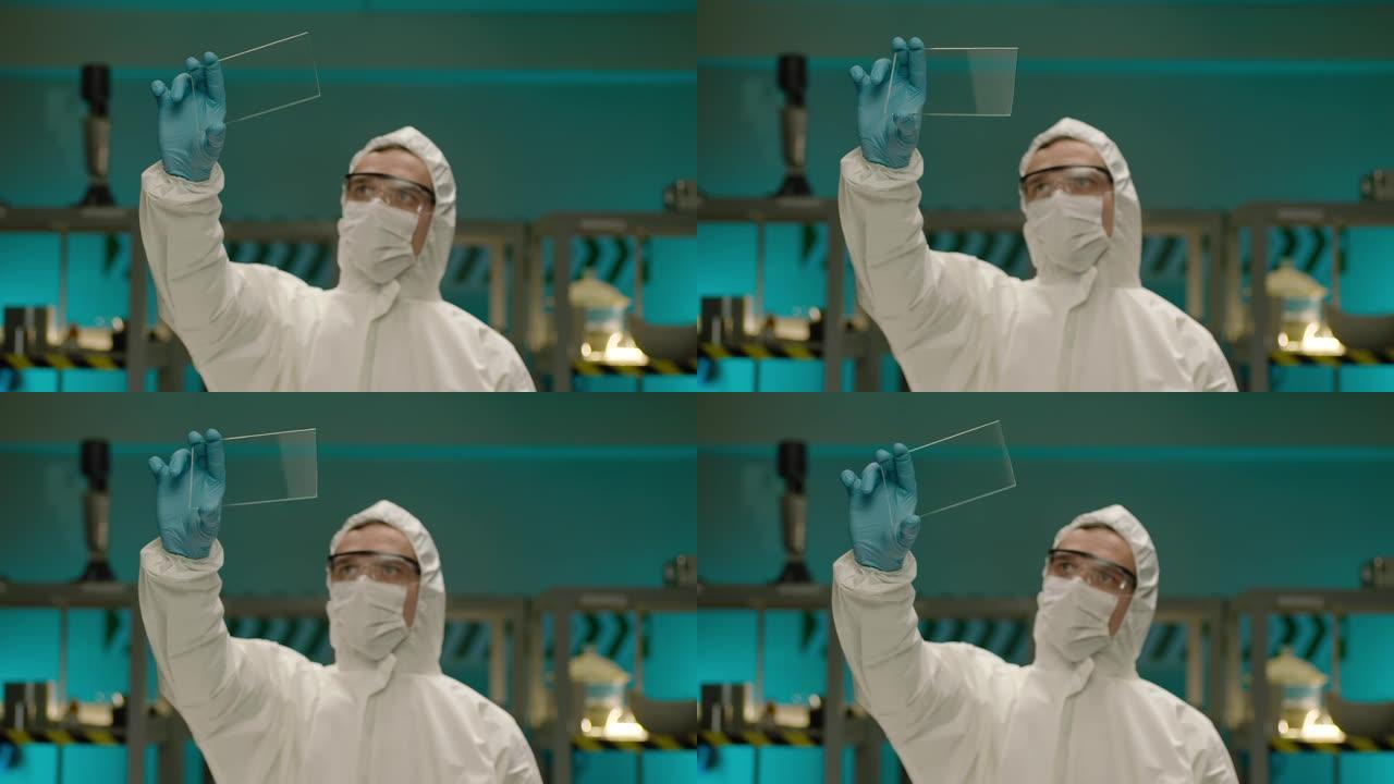 专业科学家化学家拿着和看方形玻璃。现代实验室中穿着白色防护服的男科学家肖像。男子研究员手里拿着玻璃小