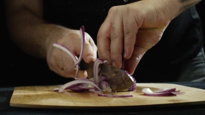在餐厅厨房慢动作中，男人的手在木板上拿着紫色洋葱的特写镜头。库存镜头。高品质食品的概念
