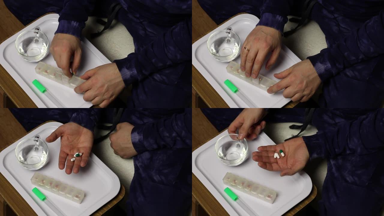 一个人从药盒里拿出一把药丸和一杯水。在他面前是一个平板电脑盒子和一个水银温度计。