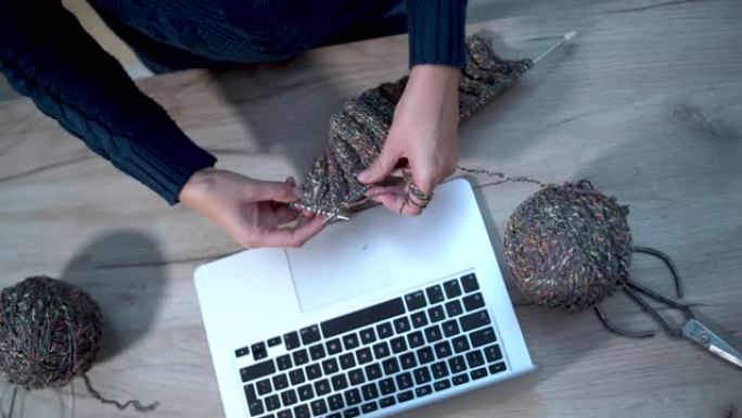 中年家庭主妇用针织纱线和针学习如何在笔记本电脑上使用网站进行针织
