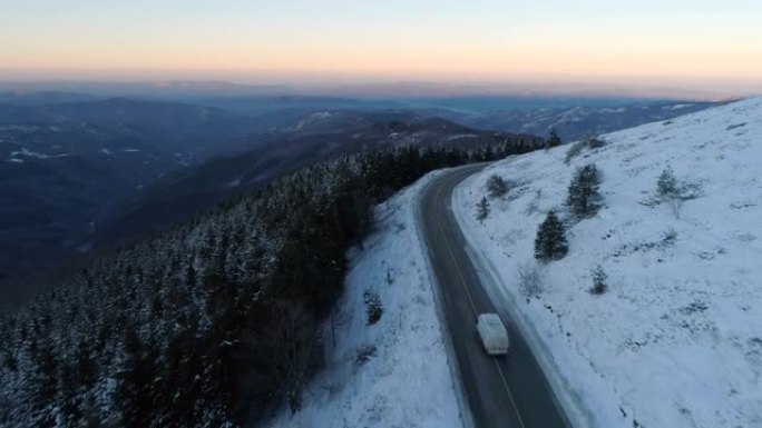 无人机跟随白色卡车槽雪山路靠近冰冻常青森林全景