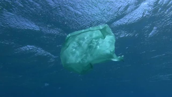 慢动作，旧的绿色塑料袋在蓝色的水面下慢慢漂移。海洋的水下塑料污染。塑料垃圾环境污染问题
