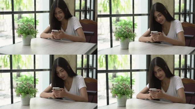 美丽的亚洲女人在咖啡馆使用智能手机。她使用智能手机以微笑和快乐的方式检查社交媒体。选择聚焦镜头