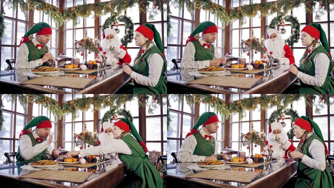两个有趣的精灵和圣诞老人坐在圣诞节背景的节日餐桌上。