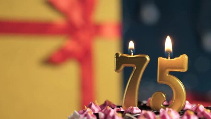 生日蛋糕75号点火器燃烧的金色蜡烛，蓝色背景礼物黄色盒子用红丝带绑起来。特写和慢动作