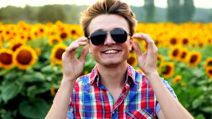 凉爽时尚的现代男性农民在向日葵的背景下戴上眼镜，微笑着