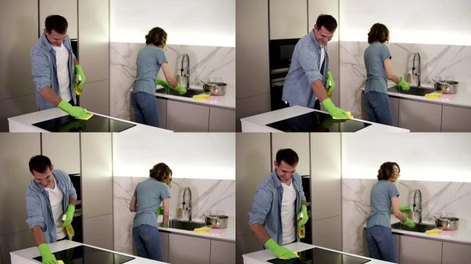 年轻的微笑已婚夫妇穿着休闲服装，都穿着绿色手套清洁厨房后搬到新家，家庭。女人正在洗碗，男人正在用拖把
