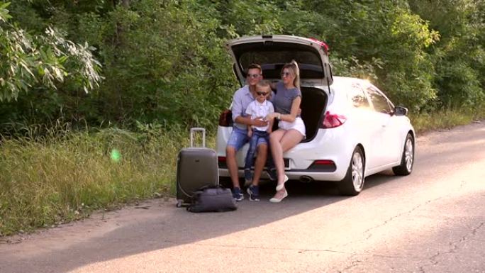 有儿子的父母坐在空旷的道路上的汽车后备箱中。家人在度假。