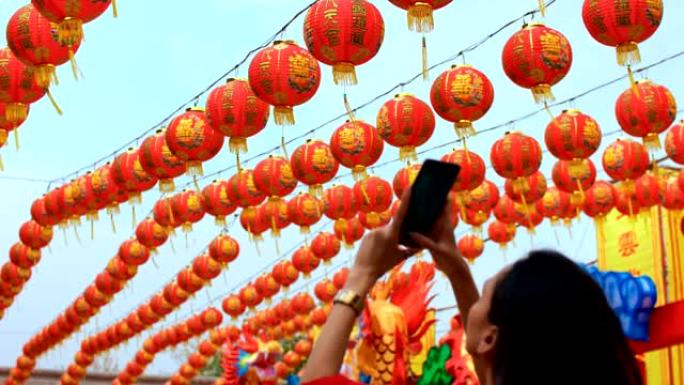 女人在神社为许多中国灯笼拍照。灯笼上的祝福文字含义有财富和幸福