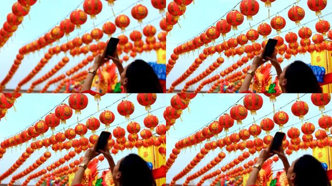 女人在神社为许多中国灯笼拍照。灯笼上的祝福文字含义有财富和幸福