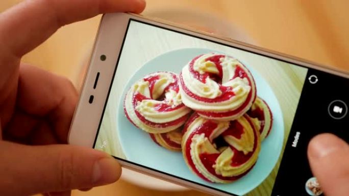 手机上手工制作甜蜜甜点照片的特写。男性在智能手机上的照片木制桌子上的圆形软饼干关闭。