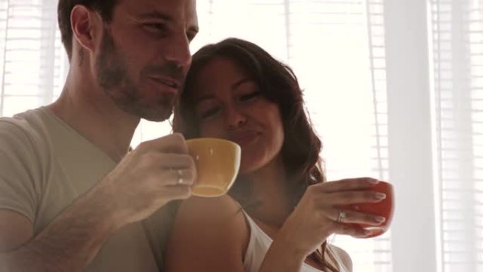 幸福的夫妻在拥抱的阳光窗前享受早晨的咖啡