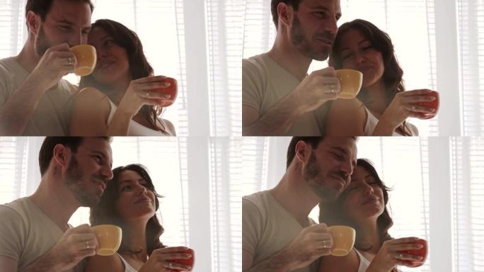 幸福的夫妻在拥抱的阳光窗前享受早晨的咖啡