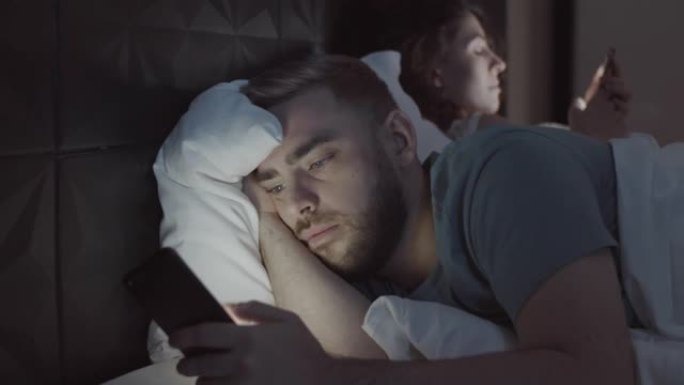 冷漠的年轻人和妻子晚上在床上使用智能手机